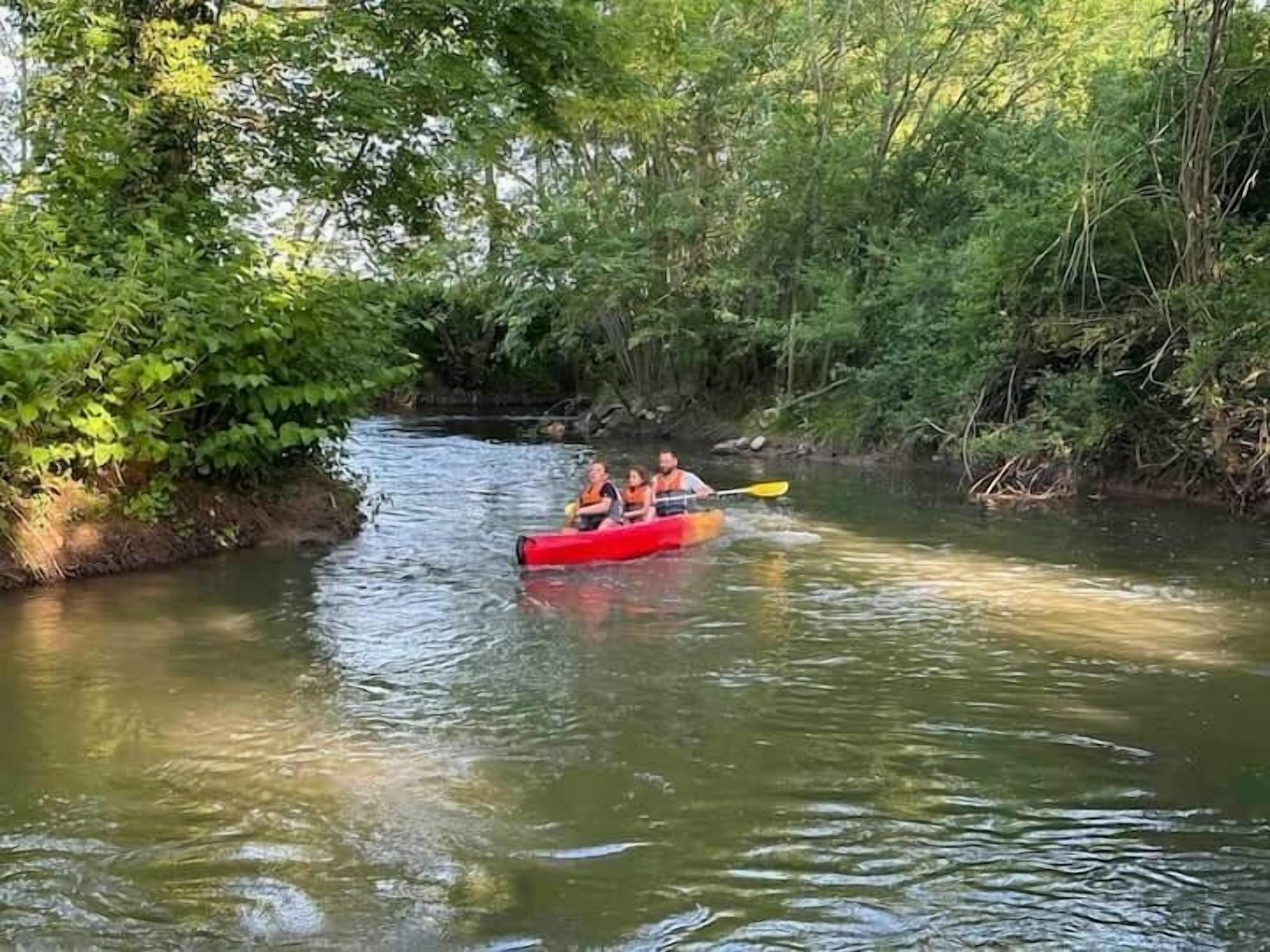 Kayak rojo con dos personas remando en un río tranquilo rodeado de abundante vegetación.