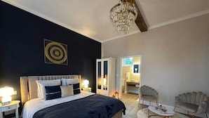 A modern bedroom with a large bed, a chandelier, a vanity, and a seating area. - L’Agate bleue (suite) (Crécy-sur-Serre)
