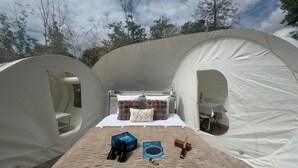 A tent with a bed, a small table, and a chair. There are binoculars, a box, and a book on the bed. - La bulle LOVE (chauffée) Au Domaine Du Pré Dieu (Crécy-sur-Serre)