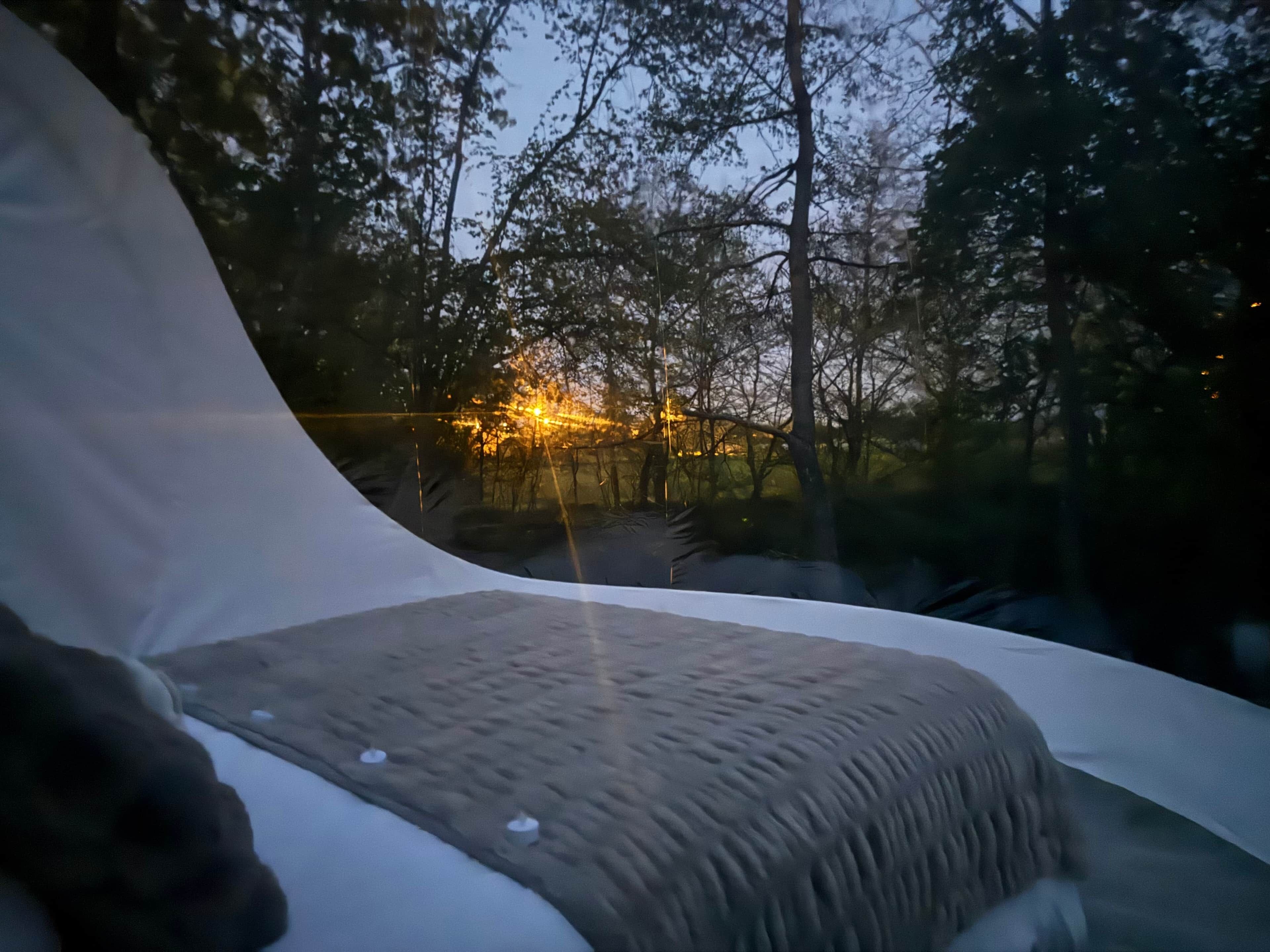 A tent with a view of trees and a distant light source.