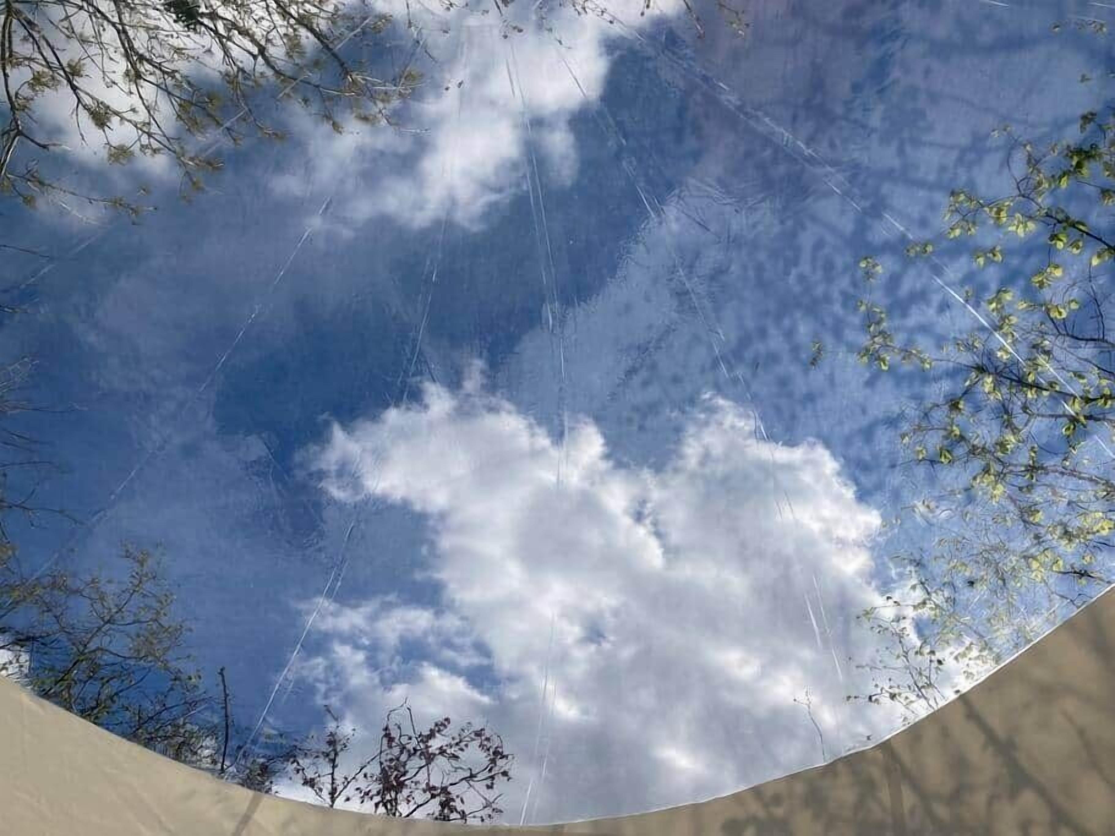 En klar himmel med moln och kala trädgrenar.