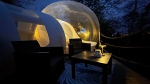 A transparent dome structure with a table and chairs in front, surrounded by a deck. - La bulle LOVE (chauffée) Au Domaine Du Pré Dieu (Crécy-sur-Serre)
