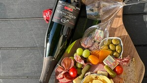 Eine Platte mit verschiedenen Wurstwaren, Käse, Oliven und Brot, begleitet von einer Weinflasche und einem Glas.