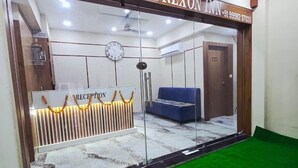 A hotel reception area with a reception desk, a clock, and a blue sofa. - Hotel Nexon Inn (Ahmedabad)