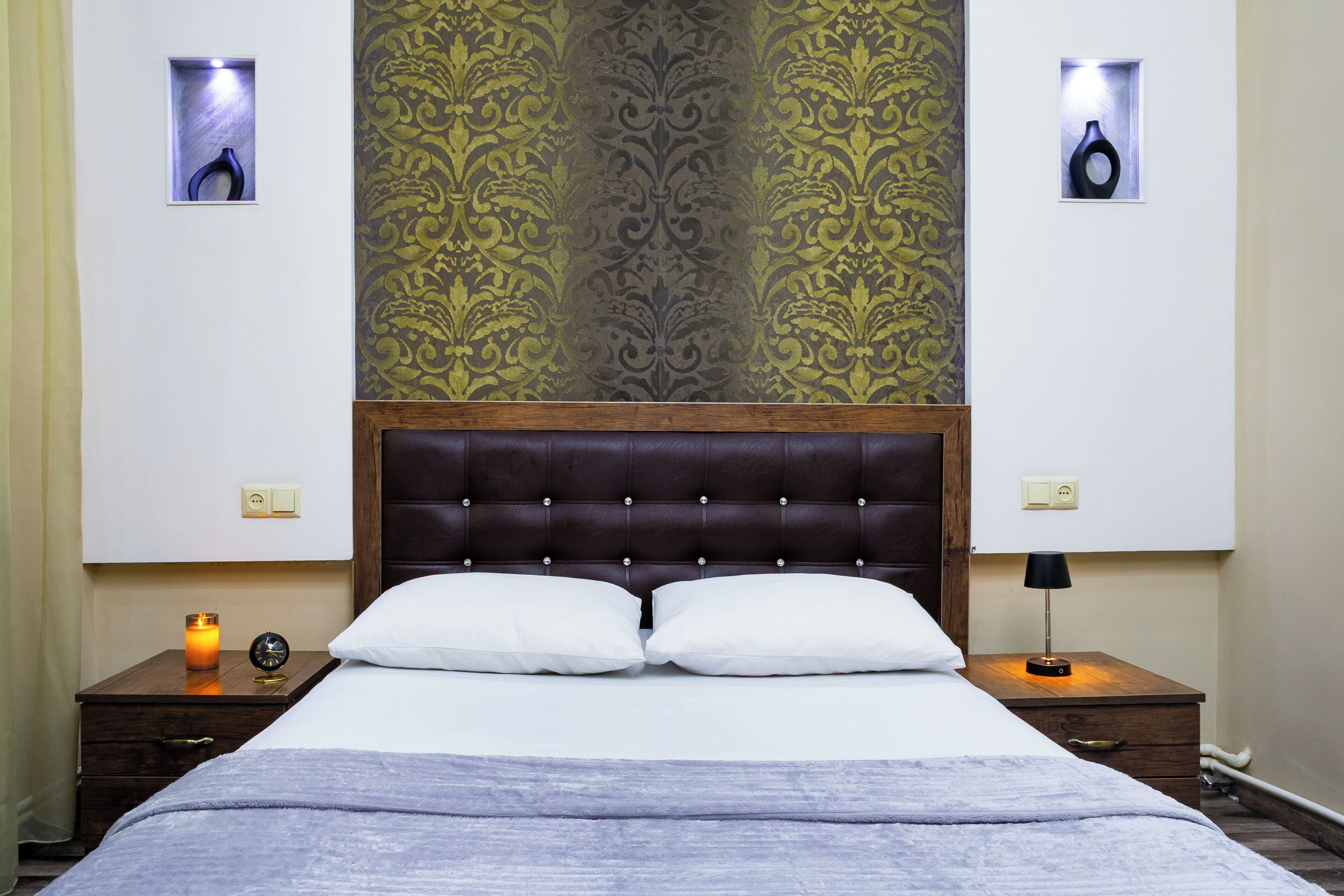 Ein ordentlich bezogenes Bett mit weißen Leinen, zwei Nachttische mit Lampen und eine Wand mit floralem Dekor.