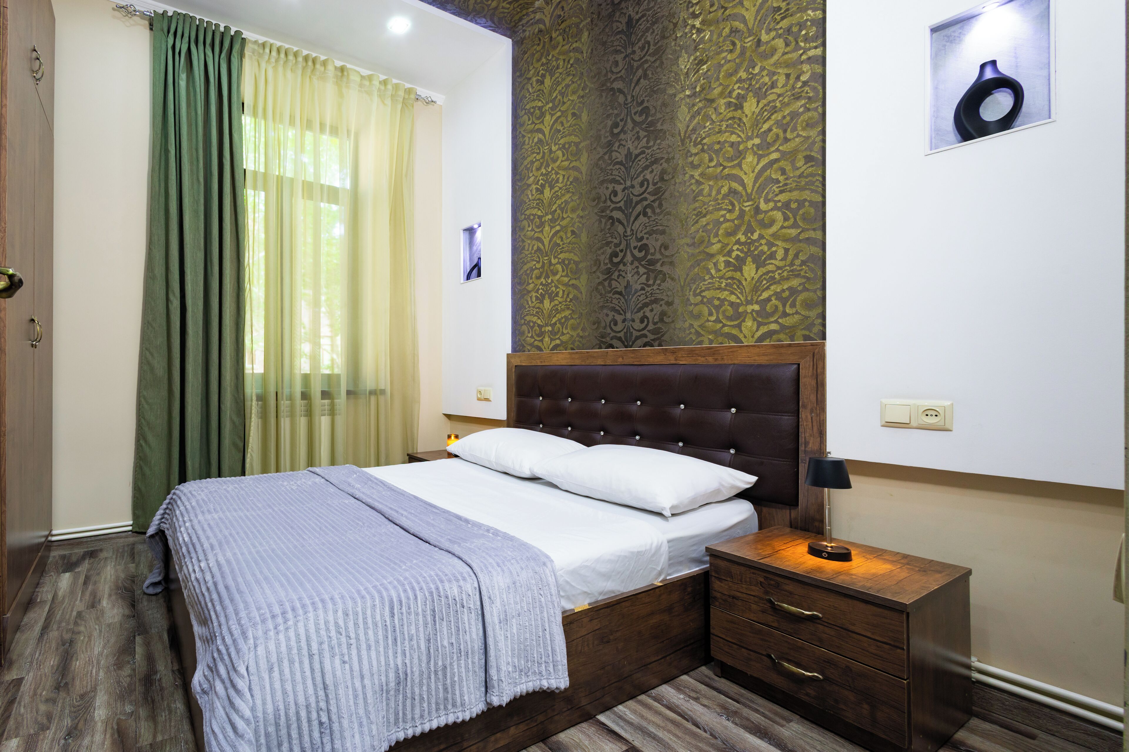 A bedroom with a wooden bed, a nightstand, a lamp, and a patterned wallpaper.