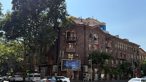 A multi-story building with a large billboard on the ground floor, parked cars, and trees.