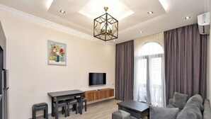 A modern living room with a sofa, a TV, a dining table, and a painting on the wall.