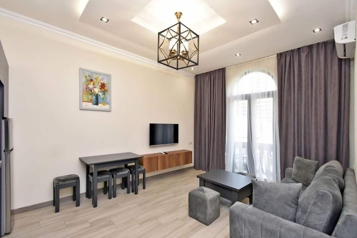 Ein modernes Wohnzimmer mit einer Couch, einem Fernseher, einem Esstisch und einem Bild an der Wand.