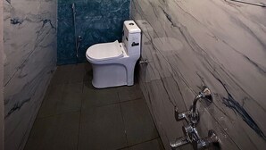 A modern bathroom with a white toilet, a shower, and a marble wall. - AR signature Inn (Mysore)