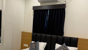 A neatly made bed with a dark headboard, white bedding, and decorative pillows. An air conditioning unit is mounted above the bed. - AR signature Inn (Mysore)