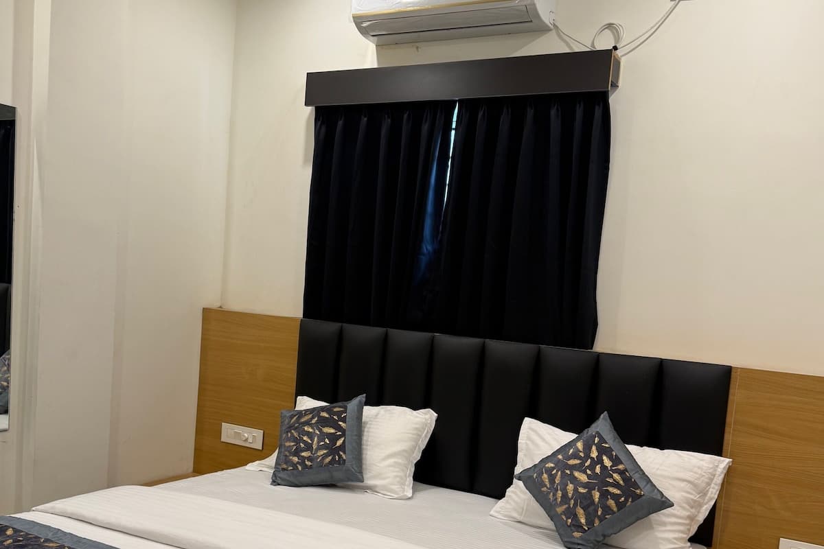 A neatly made bed with a dark headboard, white bedding, and decorative pillows. An air conditioning unit is mounted above the bed.