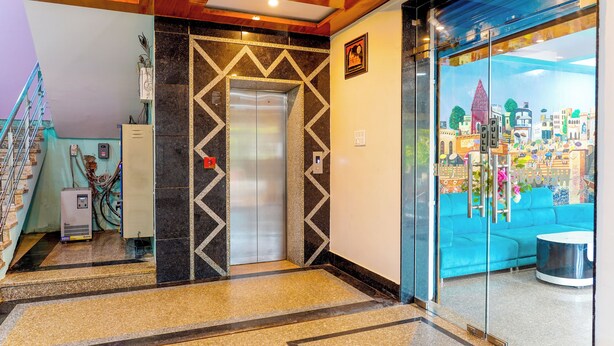 Een lift met een geometrisch wandontwerp, een blauwe bank en een glazen wand met uitzicht op de stad.