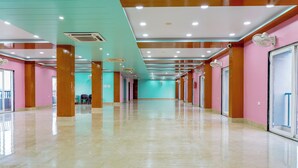 Een ruime hotelgang met teal- en roze wanden, houten pilaren en een glanzende betegelde vloer.