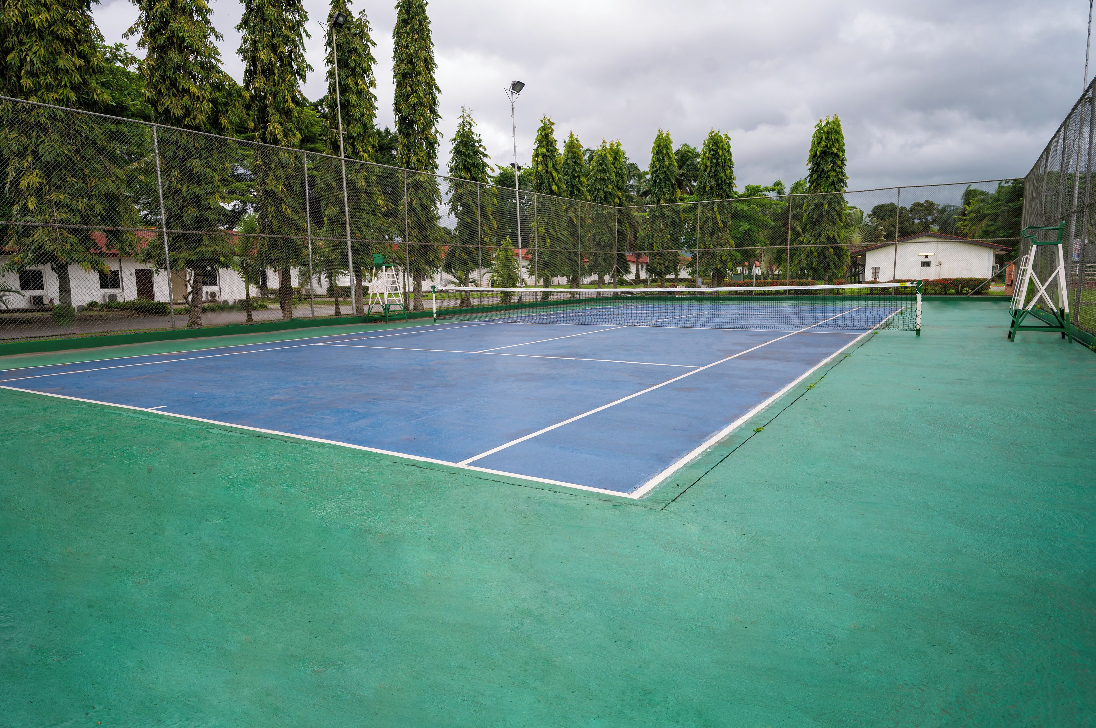 Un court de tennis avec un filet, entouré d’une clôture et d’arbres.