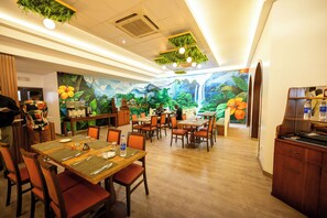 A restaurant with wooden tables and chairs, a mural of a tropical scene, and hanging greenery on the ceiling. - Heliconia Park Hotel & Golf Resort (Port Harcourt)