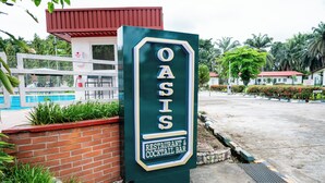A sign for Oasis Restaurant & Cocktail Bar with a pool in the background. - Heliconia Park Hotel & Golf Resort (Port Harcourt)