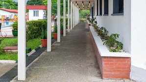 A covered walkway with hanging lights, potted plants, and a view of a pool and buildings in the background. - Heliconia Park Hotel & Golf Resort (Port Harcourt)
