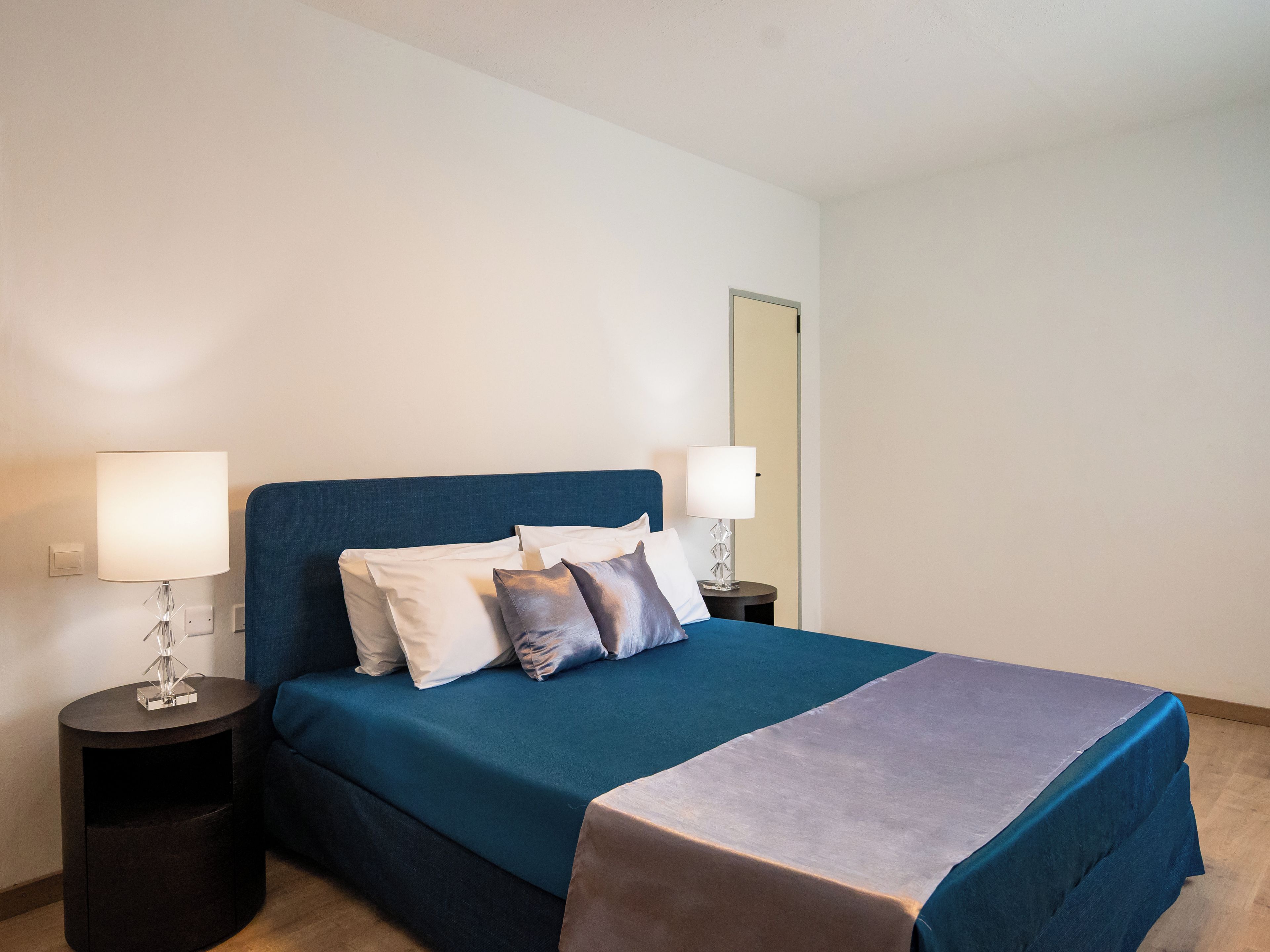 A neatly made bed with a blue headboard, two bedside tables with lamps, and a mirror on the wall.