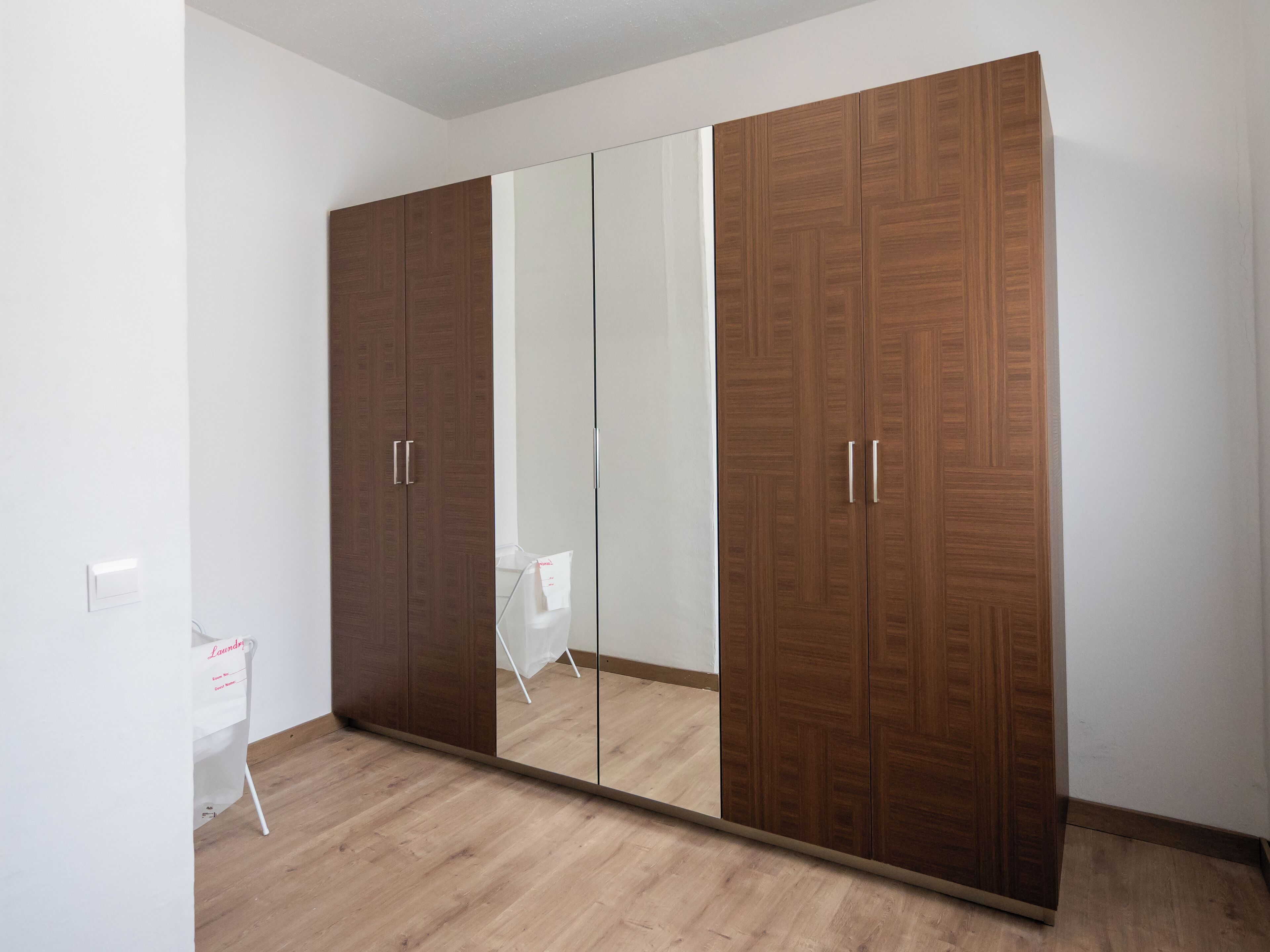 A room with a large wardrobe, a mirror, and a small desk with a white chair.
