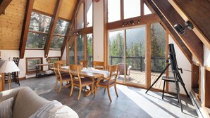 Ein geräumiges Zimmer mit einem Holztisch, Stühlen und einem Deckenventilator. Große Fenster bieten Ausblicke ins Freie.