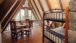 Ein Schlafzimmer im Loft-Stil mit Etagenbett, Holztisch, Stühlen und Blick ins Freie.