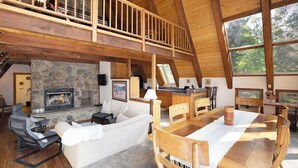 Ein geräumiges Wohnzimmer mit Kamin aus Stein, Holzbalken an der Decke und einem Esstisch mit Stühlen.