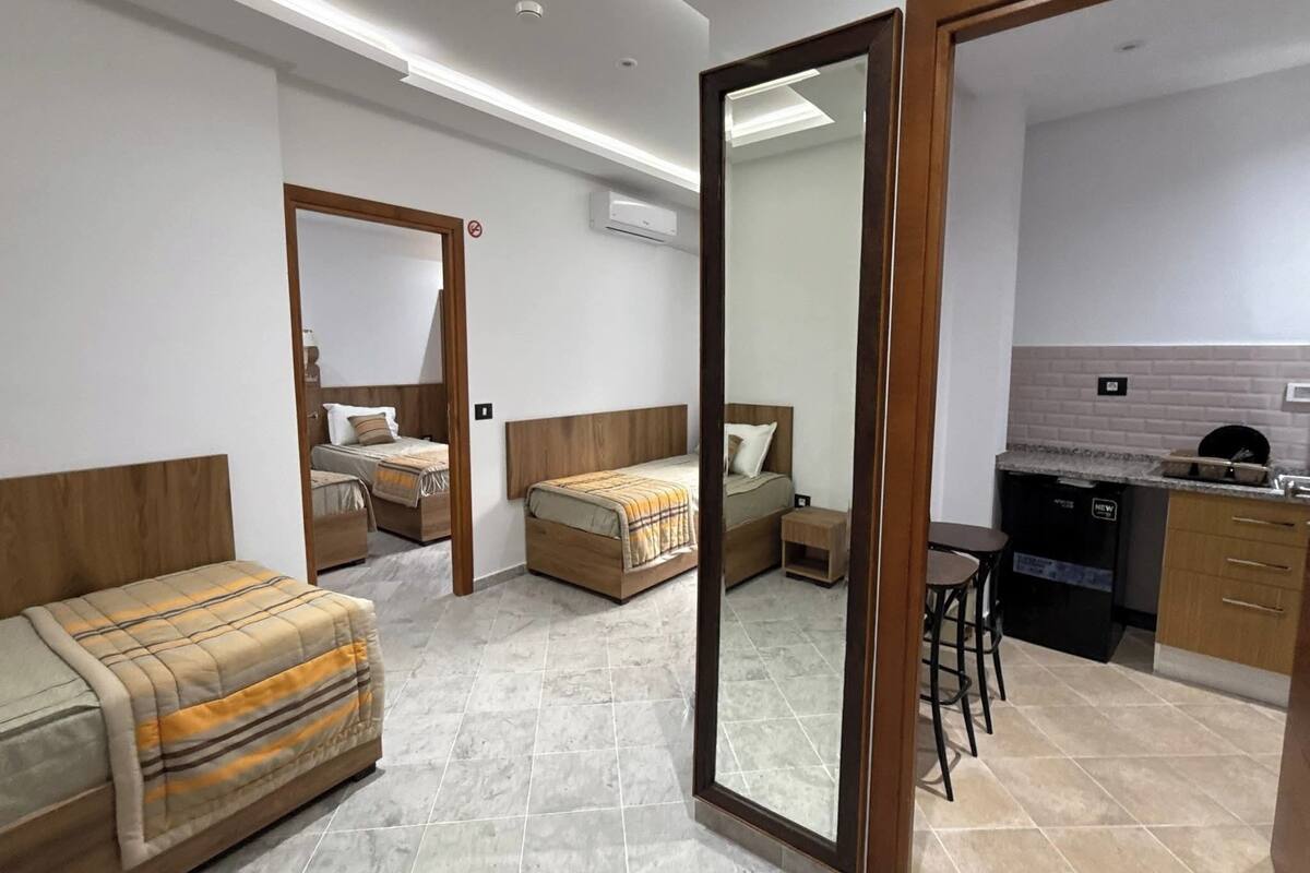 Une chambre d’hôtel moderne équipée de deux lits simples, d’un canapé, d’un petit coin cuisine et d’une salle de bain.