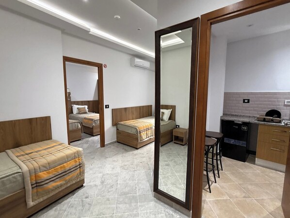 Una habitación de hotel moderna con dos camas individuales, un sofá, una pequeña cocina y un baño.