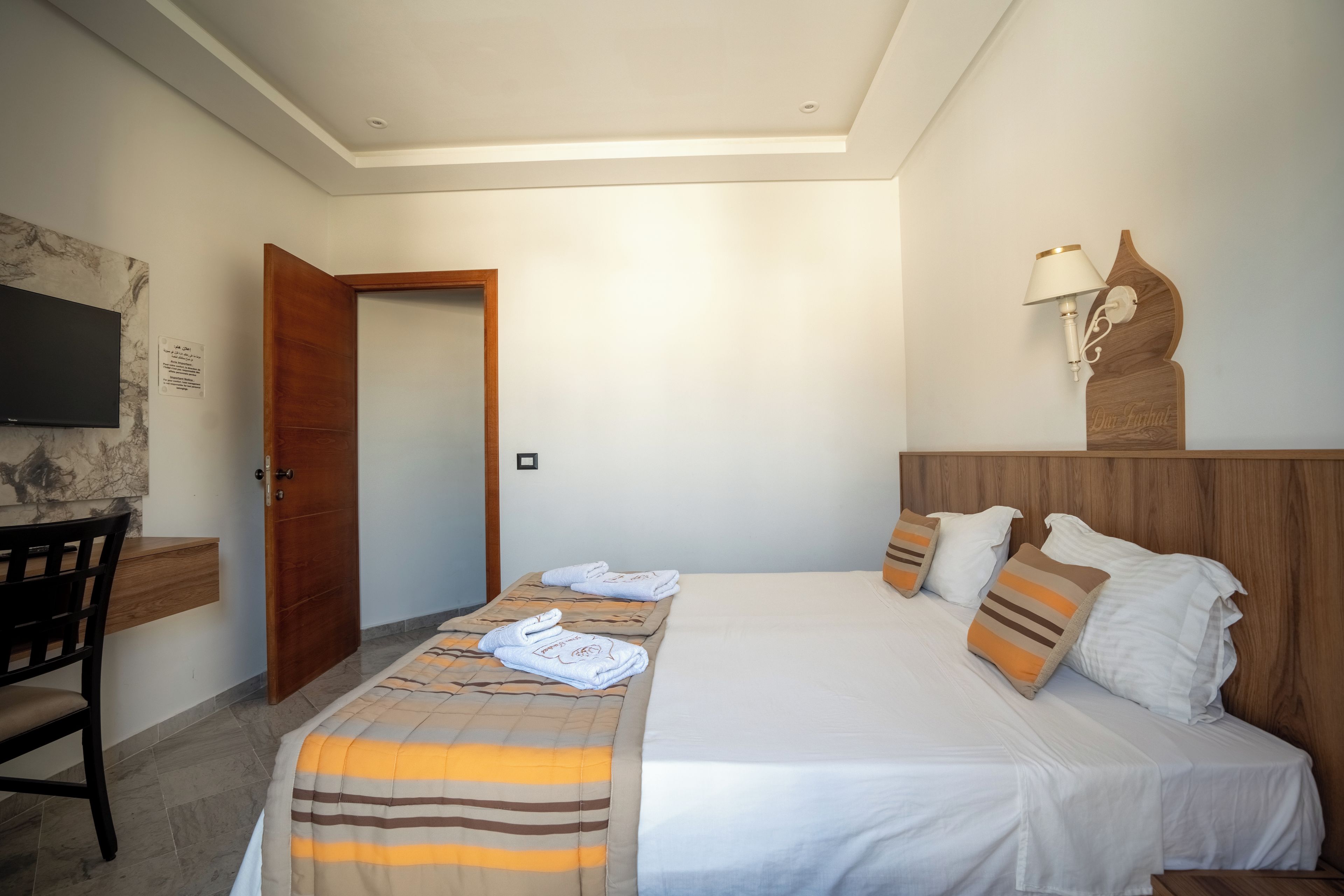 Ein Hotelzimmer mit Bett, Schreibtisch, Fernseher und einem hölzernen Kopfteil.