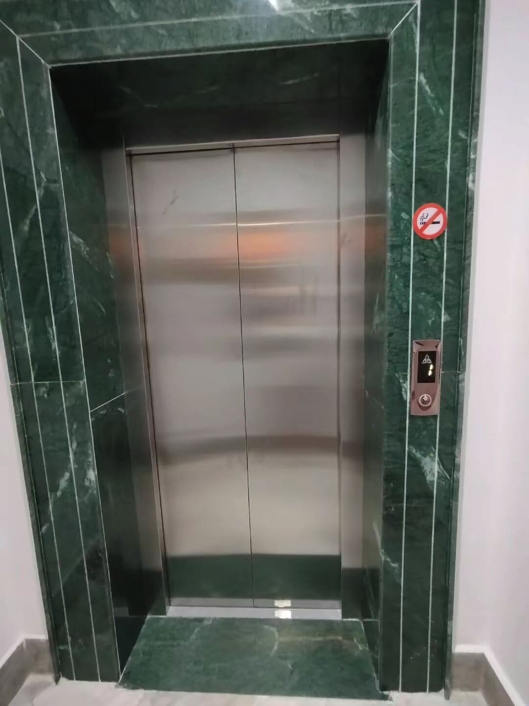 An elevator with a metallic interior and green marble walls.