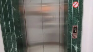 Um elevador com interior metálico e paredes de mármore verde.