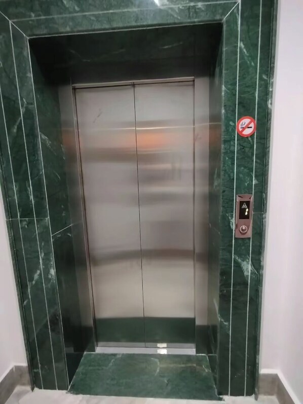 Un ascensor con interior metálico y paredes de mármol verde.