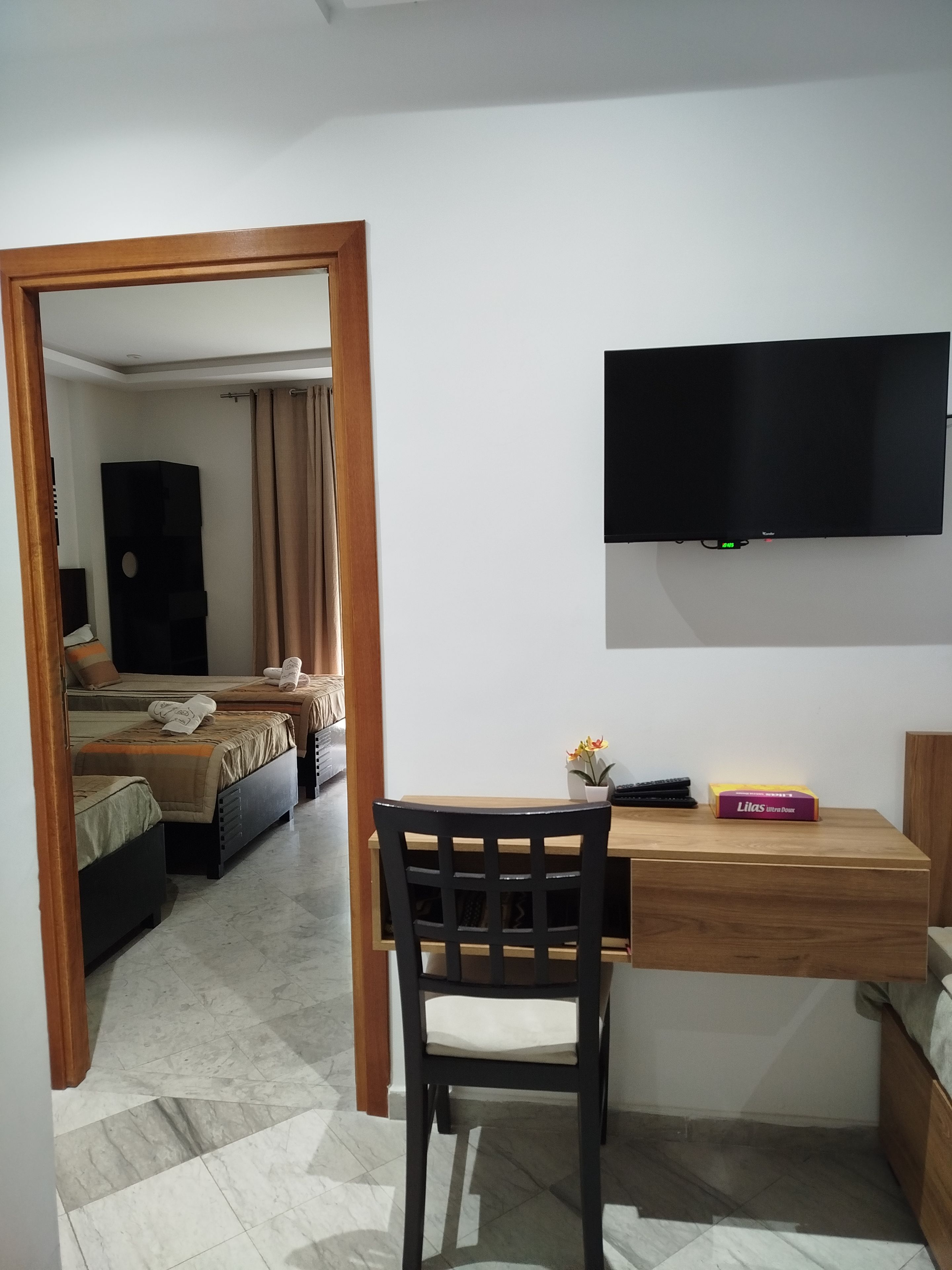 A room with a bed, a desk, a chair, a television, and a small table with a box.