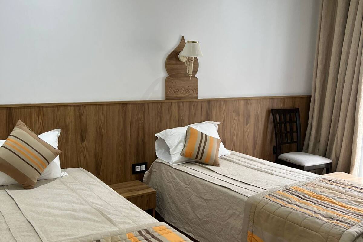Une chambre d’hôtel avec deux lits, une table de chevet, une lampe, une chaise et une fenêtre avec des rideaux.