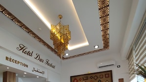 A hotel reception area with a reception desk, a wooden sofa, patterned rug, and a chandelier. - Dar Farhat Suite Hotel (Tunis)