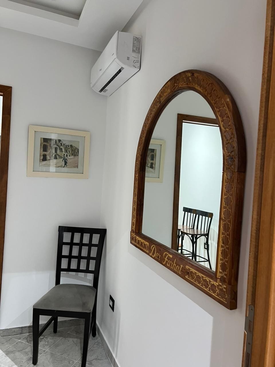 A room with a wooden-framed mirror, a black chair, and a framed picture on the wall.