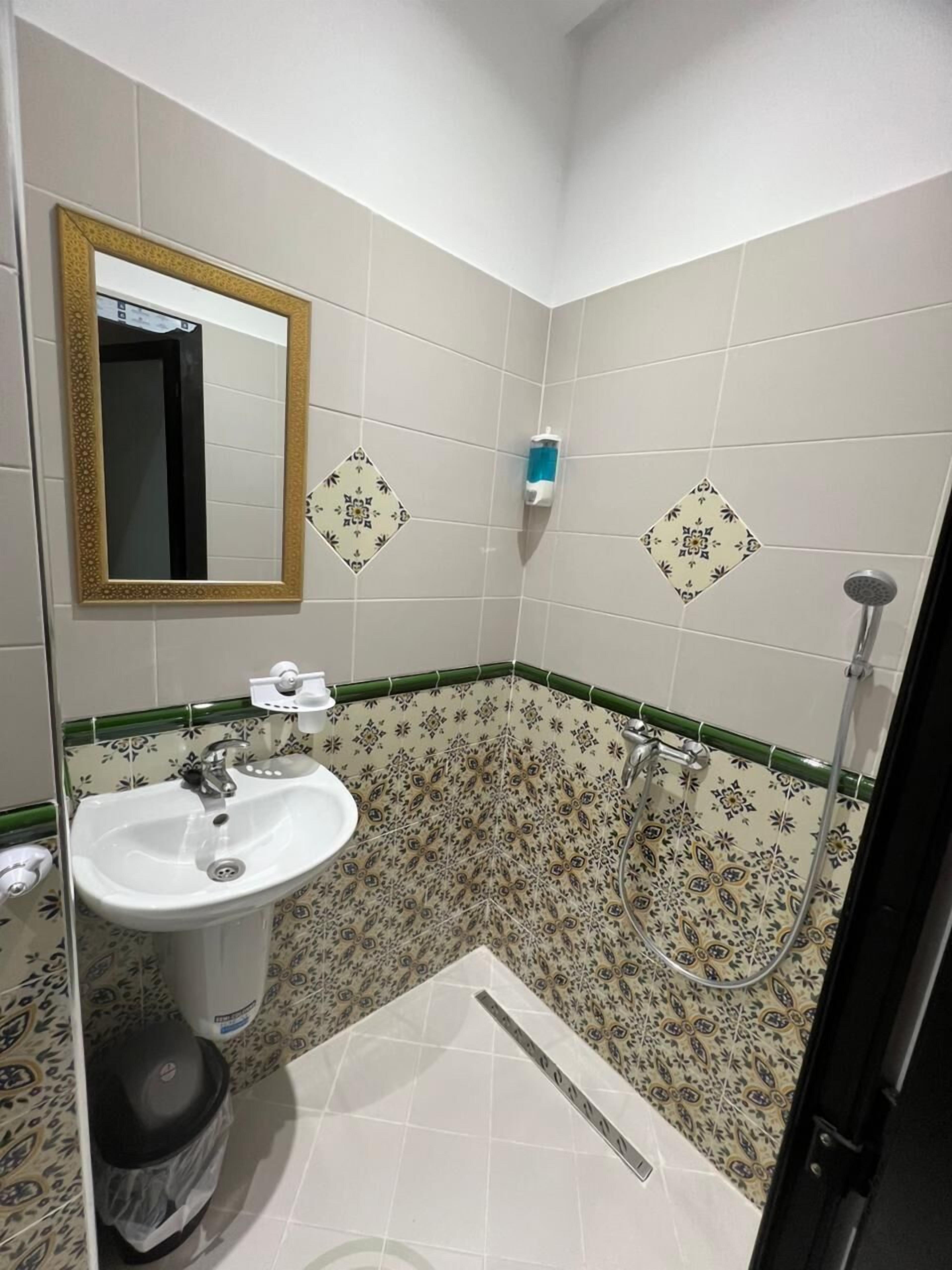 Une salle de bain avec un lavabo, un miroir, une douche et des carreaux décorés.