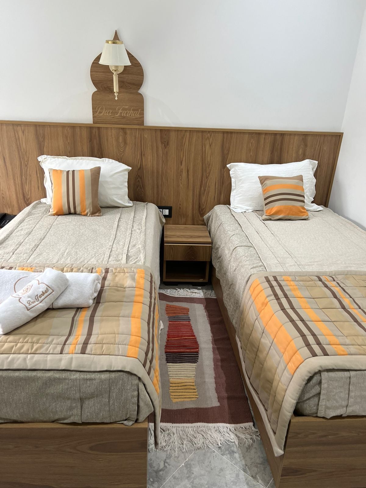 A hotel room with two beds, a nightstand, a lamp, and a decorative wall piece.