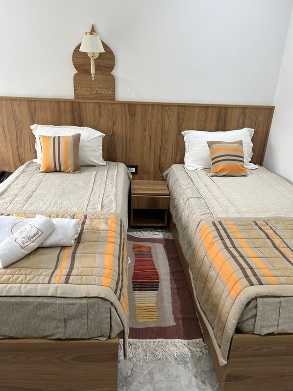 Habitación de hotel con dos camas, una mesita de noche, una lámpara y un adorno en la pared.