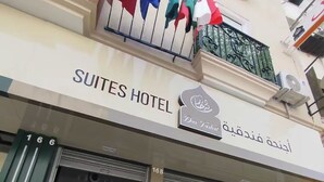 The exterior of Suites Hotel with a sign in both English and Arabic, a balcony with flags, and a wooden bench outside the entrance. - Dar Farhat Suite Hotel (Tunis)