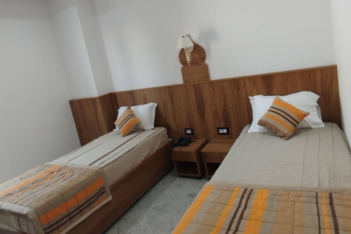 Une chambre d’hôtel avec deux lits, des têtes de lit en bois, une table de chevet, une lampe et un luminaire au plafond.
