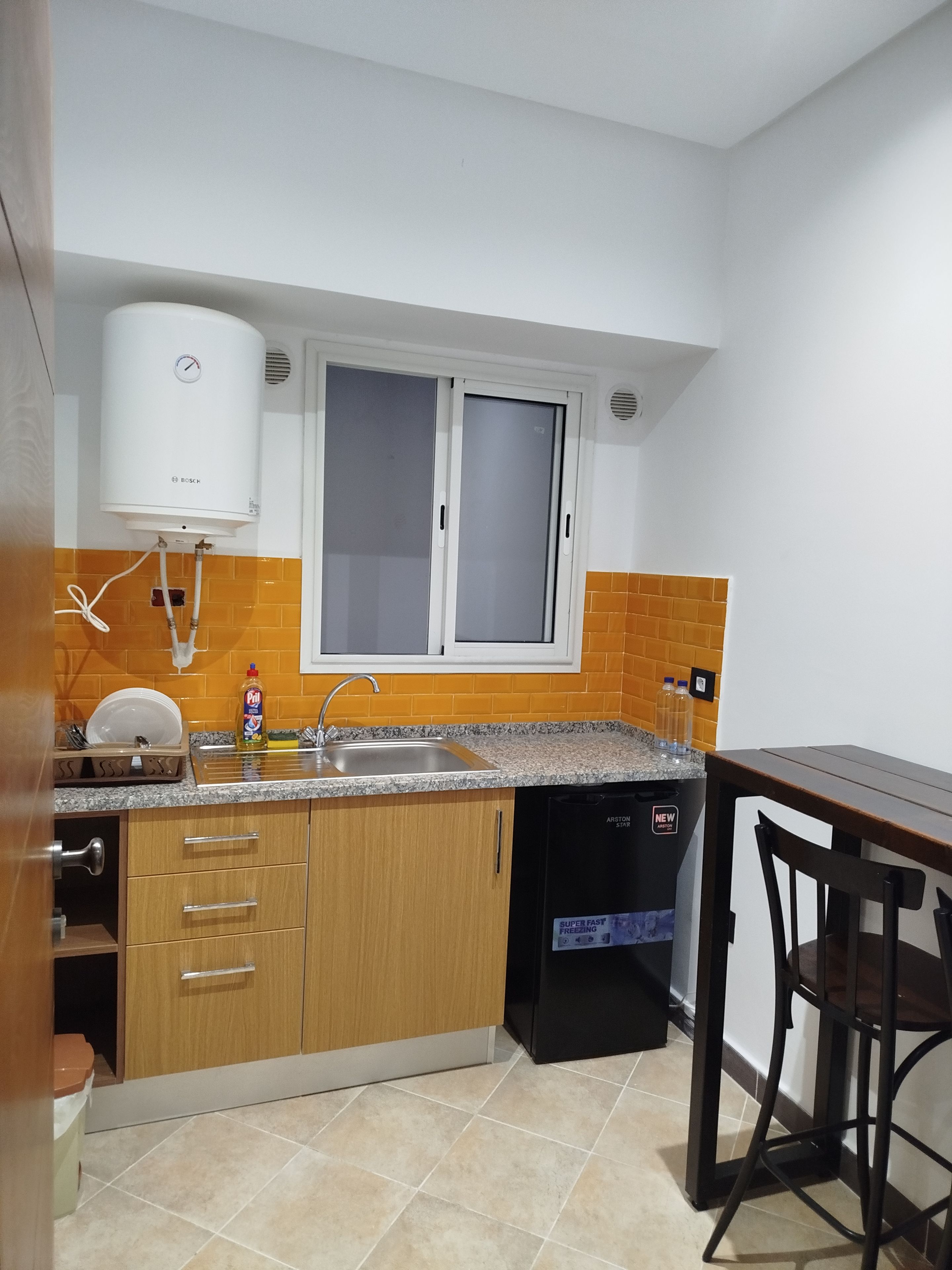 Cozinha equipada com aquecedor Bosch, pia, escorredor de louça e lava-louças preta.