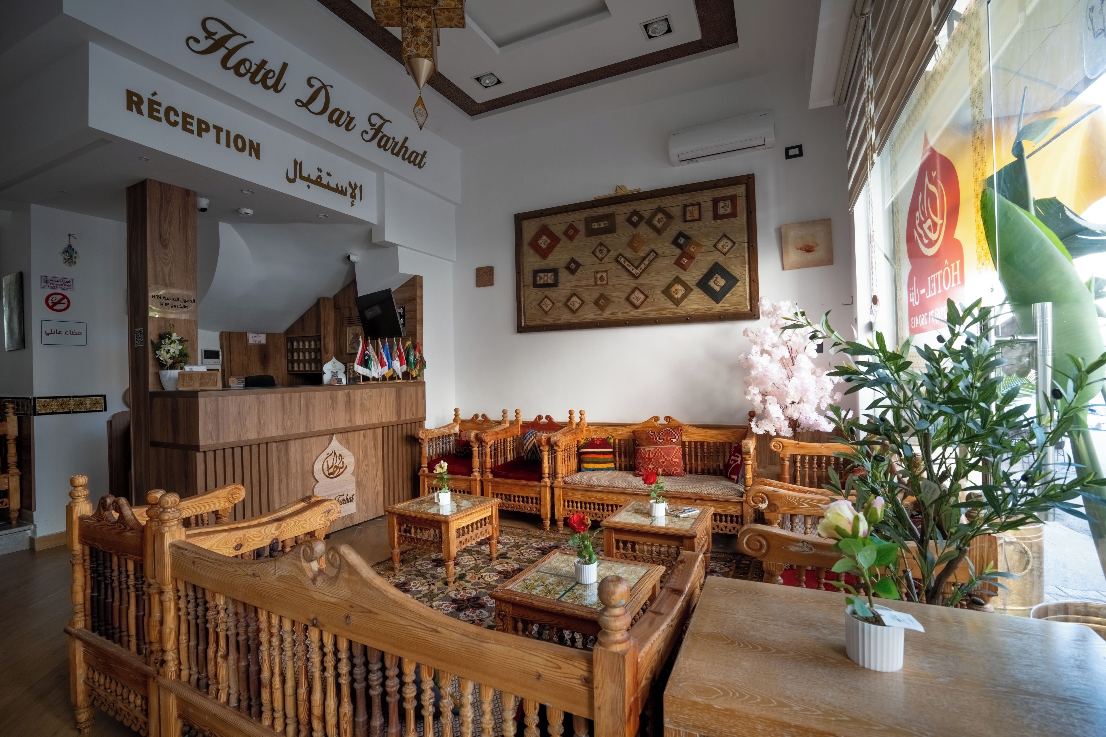 Uma área de recepção de hotel com um balcão de madeira, sala de estar com sofás de madeira e uma parede decorada com quadros emoldurados.