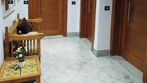 A hallway with a wooden bench, a small table with a potted plant, and three wooden doors. - Dar Farhat Suite Hotel (Tunis)