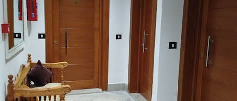 A hallway with wooden doors, a bench with a cushion, and a tiled floor.