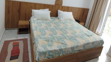 Una cama con colcha estampada con motivos de hojas, cabecera de madera, mesita de noche y velador con lámpara.