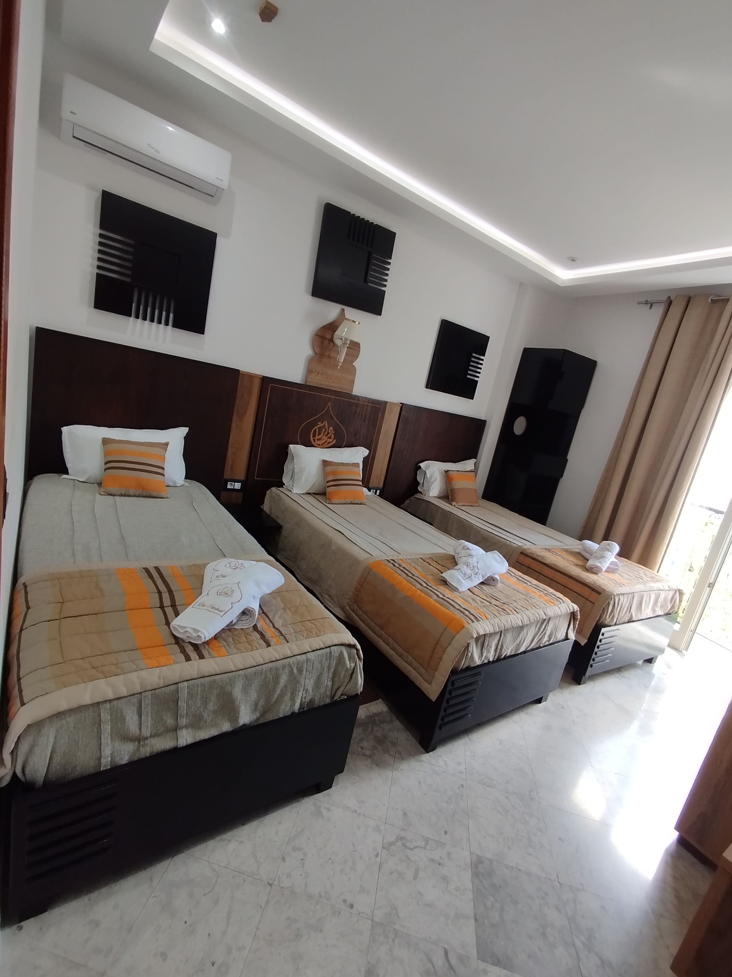 A hotel room with three beds, a ceiling-mounted air conditioner, and a modern light fixture.
