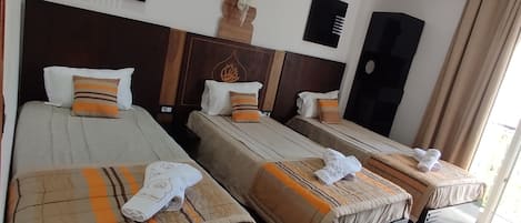 A hotel room with three beds, a ceiling-mounted air conditioner, and a modern light fixture.