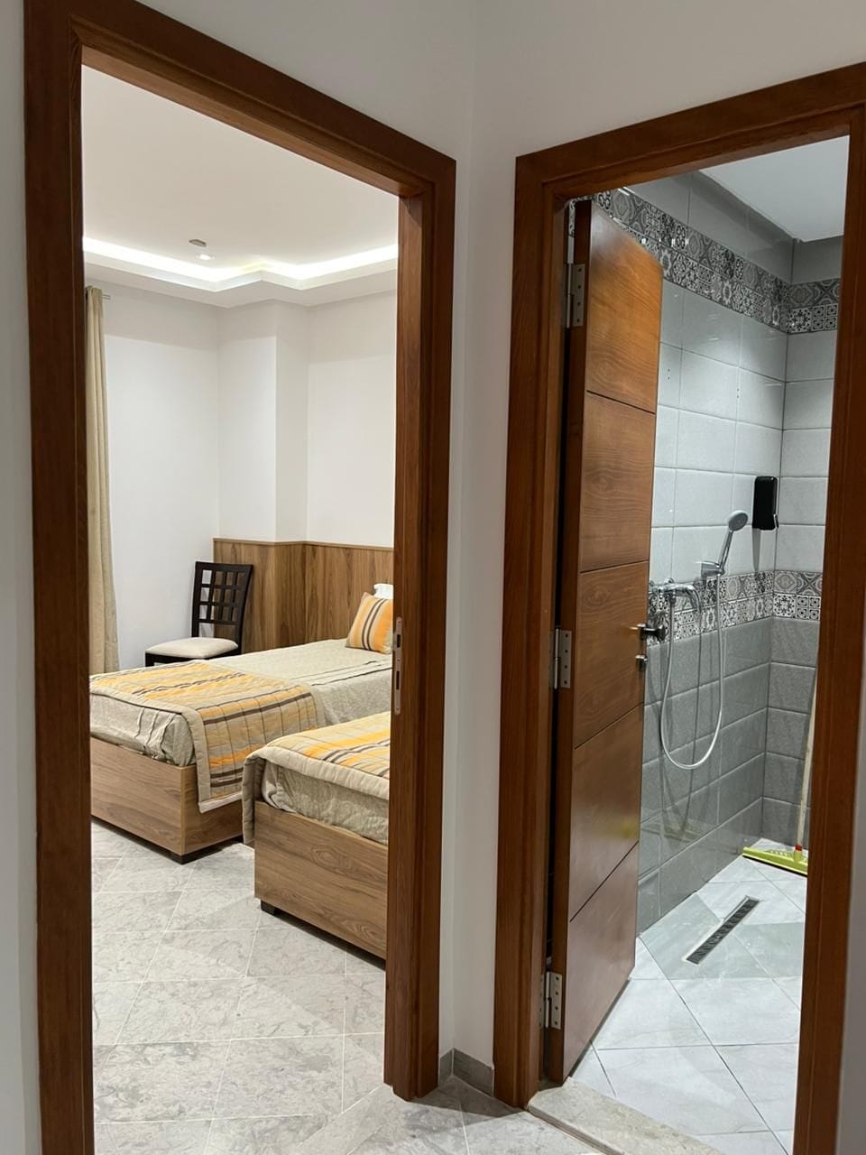 A hotel room with a bed, a wooden headboard, a shower area with a tiled wall, and a wooden door.